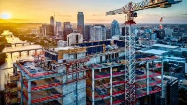 Large tower under construction with crane with American and Texas flags in downtown Austin, Texas against sunset sky.